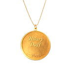 Gold coin pendant necklace engraved with Hilary Duff script and 2026, close-up front view on chain